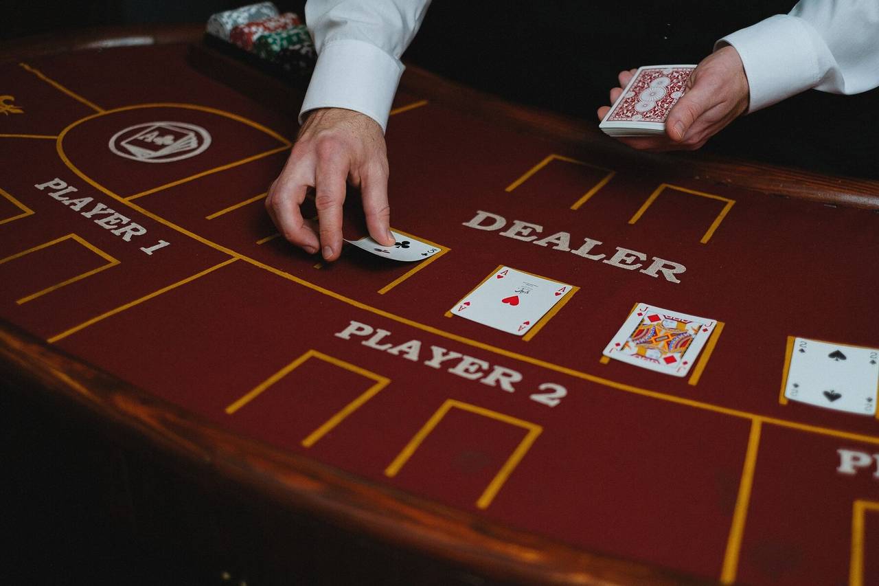Mãos do crupiê a distribuir cartas numa mesa de blackjack de feltro vermelho